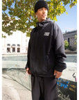 Person wearing The Stacked Jacket Black, a 10k lightweight weatherproof shell jacket, ideal for snowboarding, in an urban setting.