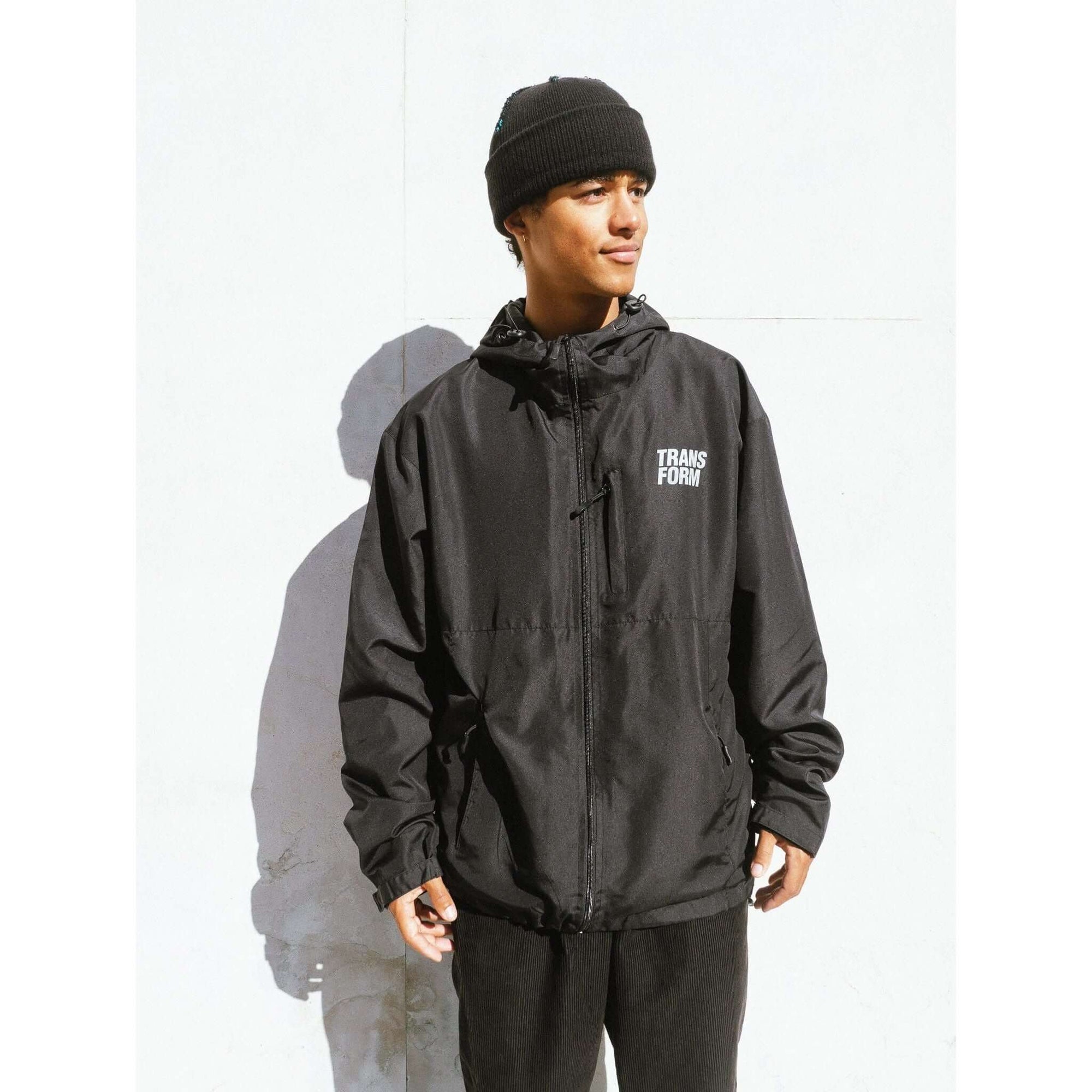 Man wearing The Stacked Jacket Black, a 10k lightweight and weatherproof shell jacket for snowboarding, with adjustable hood and zippable pockets.